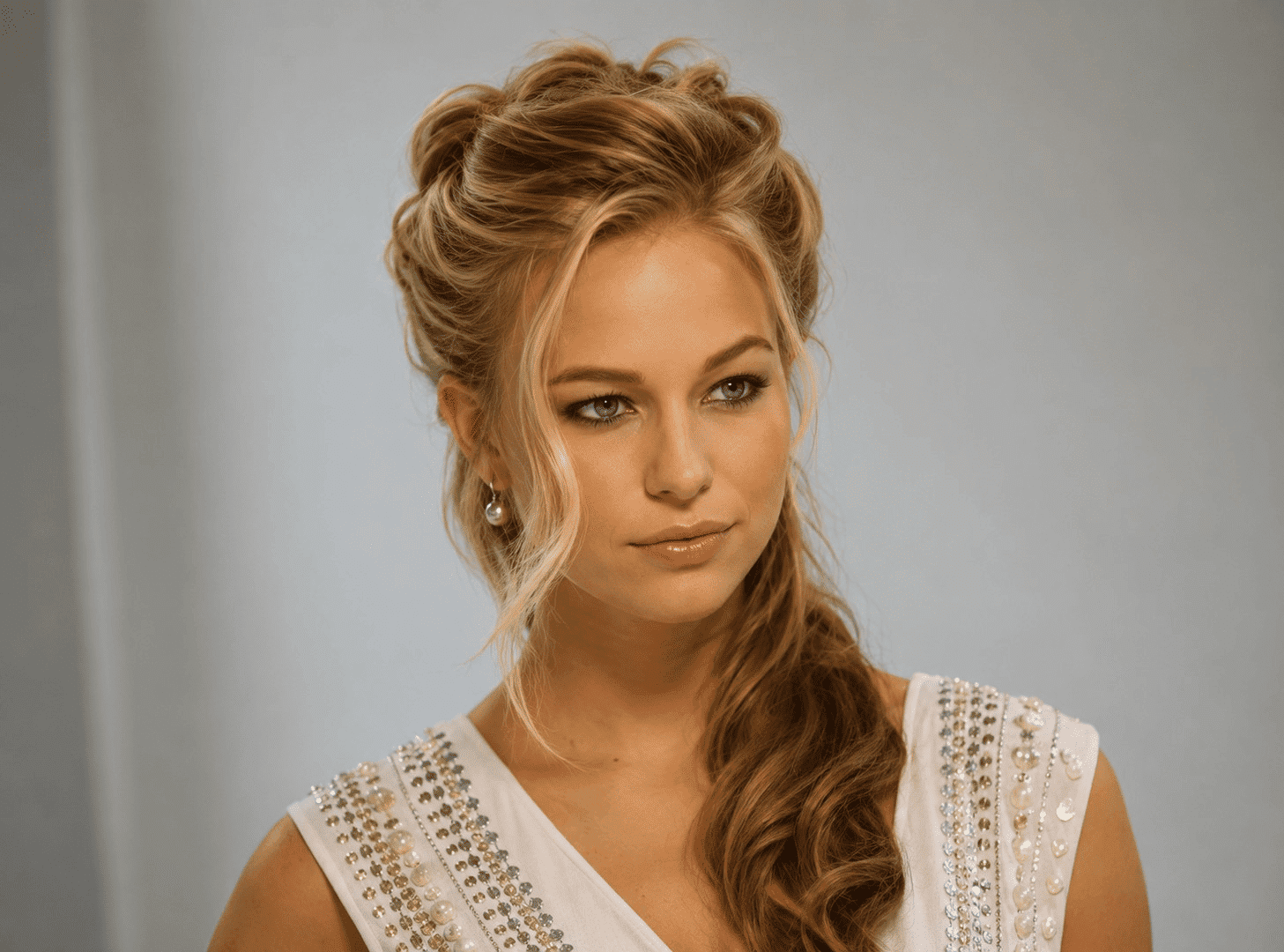 Elegant person with styled hair and embellished white attire in a portrait setting.