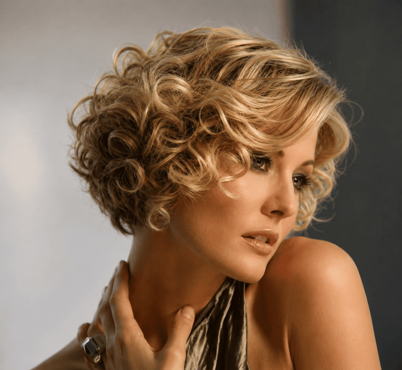 Short-haired woman with blonde curls looking sideways against a soft-focus background.